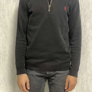 Svart tröja från Polo Ralph Lauren - Säljer en stilren svart tröja från Polo Ralph Lauren med dragkedja vid halsen och det klassiska röda logotypbroderiet på bröstet. Tröjan har långa ärmar och är perfekt för en avslappnad look. Passar bra till jeans eller chinos. Lite fel på den det ser ni på bilden 
