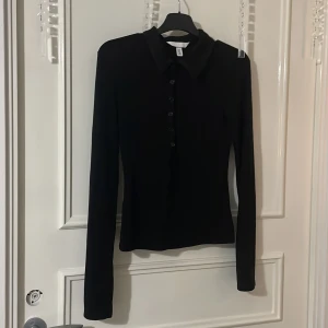 Svart långärmad tröja med knappar - Snygg svart långärmad tröja med knappar. Tröjan har en klassisk krage. Tröjan är från H&M och har inte används en endaste gång☺️