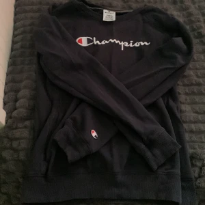 Mörkblå tröja från Champion - Säljer en skit snygg mörkblå tröja från Champion med deras ikoniska logga på bröstet och ärmen. Tröjan har långa ärmar och är perfekt för en avslappnad stil. Den är gjord i ett mjukt material som känns skönt mot huden. Den har även en ficka som går från ena sidan till andra på framsidan