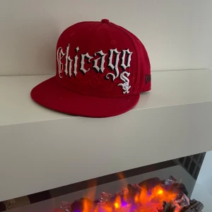 Röd keps med broderad text - Snygg röd keps med broderad text 'Chicago' i vitt och svart. Märke på sidan och MLB-logga bak. Perfekt för att ge din outfit en cool touch.