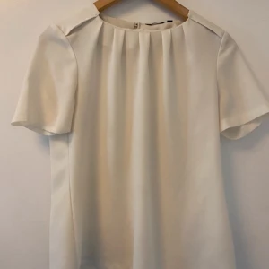 Vit blus - Elegant vit blus med korta ärmar och rund halsringning. Perfekt för en stilren look. Blusen har en enkel och klassisk design som passar till många olika tillfällen.