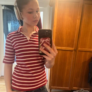 Röd- och vitrandig pikétröja - Säljer en snygg röd- och vitrandig pikétröja med krage. Tröjan har korta ärmar och en klassisk design som passar perfekt för en avslappnad stil. Perfekt för dig som gillar en sportig look! Tröjan är lite nostalgisk då den påminner av polan&pyret💕