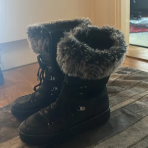 Svarta vinterboots med fuskpäls - Snygga svarta vinterboots med grå fuskpäls runt skaftet. Skorna har snörning och dragkedja för enkel på- och avtagning. Perfekta för kalla vinterdagar.
