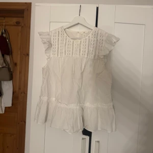 Vit blus från H&M - Säljer en söt vit blus från H&M i storlek M. Den har spetsdetaljer på överdelen och volangärmar. Blusen har en volangkant nedtill💕