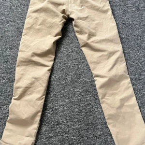 Beige chinos från Carhartt - Snygga beige chinos från Carhartt med klassisk design. Byxorna har en rak passform och är tillverkade i ett slitstarkt material. Perfekta för en stilren look.