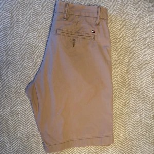 Tommy Hilfiger shorts  - Snygga beige shorts från Tommy Hilfiger med klassisk design. De har en knapp och dragkedja framtill samt en broderad logga på bakfickan. Perfekta för en avslappnad stil.