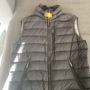 Svart dunväst från Parajumpers - Säljer en svart dunväst från Parajumpers i superlätt material. Västen har dragkedja framtill och två fickor med dragkedjor. Perfekt för kyliga dagar med sin quiltade design och höga krage.  STORLEK: S. COND:  8/10