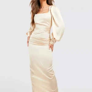 Boohoo satin klänning - Elegant långklänning i champagnefärg med puffiga långa ärmar och en stilren fyrkantig urringning. Klänningen har en smickrande slits på sidan och är tillverkad i ett glansigt material som ger en lyxig känsla. Endast testad storlek S men kan användas som M också 
