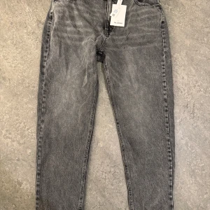 Grå jeans från Pull&Bear - Snygga grå jeans från Pull&Bear med en klassisk femficksdesign. De har en knappgylf och är tillverkade i ett slitstarkt denimtyg. Perfekta för en avslappnad stil. De är oanvända och är strl 46