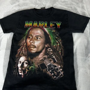 Bob Marley - Cool svart t-shirt med färgglatt Marley-tryck. Perfekt för musikälskare som vill ha en avslappnad stil. T-shirten har korta ärmar och en rund halsringning.