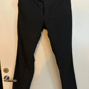 Svarta kostymbyxor - Snygga svarta kostymbyxor med en elegant passform. Perfekta för en stilren look. Byxorna har en klassisk design med dragkedja och knappar framtill. Storlek 31/32