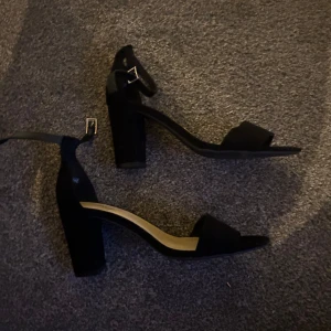 Svarta klackskor med remmar - Snygga svarta klackskor från Alley med remmar runt ankeln och öppen tå. Perfekta för en stilren look med en bekväm blockklack.