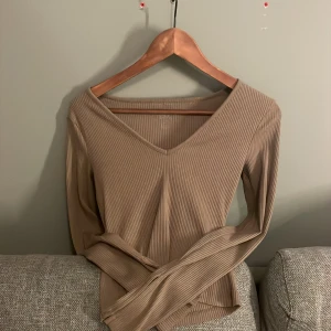 Beige ribbad tröja - Säljer en stilren beige ribbad tröja med v-ringning. Tröjan har långa ärmar och en mjuk, bekväm passform. Perfekt för en avslappnad look.