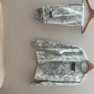 Blå och vit mjukis sätt med tryck - Säljer en grå och vit batikmönstrad sweatshirt med texttryck på bröstet. Tröjan har långa ärmar och ribbade muddar vid ärmslut och nederkant. Perfekt för en avslappnad stil. är det storlek 170 14 år men skulle kunna passa en Xs. på armen av tröjan så finns det en liten gul fläck som knappt syns