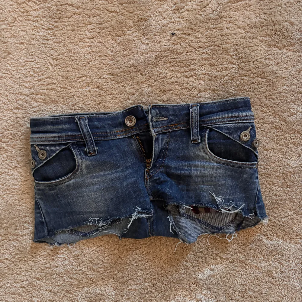 Säljer ett par fina lågmidjade jeansshorts i mörkblå denim med slitna kanter och snygga slitningar. Perfekta för sommaren 😍❤️pris kan diskuteras 🥰. Shorts.