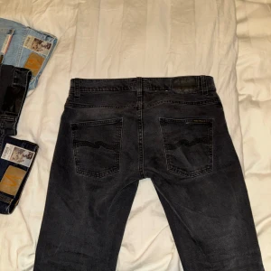 Nudie Jeans Grim Tim - Säljer ett par grå/svarta jeans från Nudie Jeans i bra skick. De har en klassisk femficksdesign med knappgylf och är i en snygg tvättad grå/svart färg. Perfekta för både vardag och fest! 🕺De är sparsamt använda med inga defekter! Storleken är 31/32 och modellen är Grim Tim! Hör av er om ni har några frågor