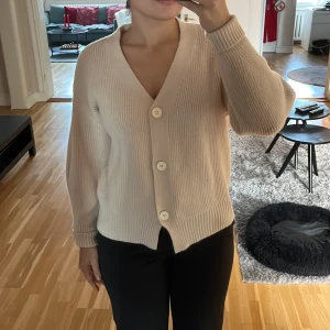Beige kofta från Shein - Mysig beige kofta från Shein i ribbat stickat material som inte sticks. Den har stora vita knappar framtill och en v-ringad design. Perfekt för höst och vår när du vill ha något varmt och stilrent 🌟Det står ingen storlek men jag skulle gissa på att det är storlek S. 