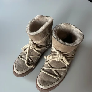 Beige vinterboots från Inuikii - Säljer ett par snygga och varma beige vinterboots från Inuikii. De är i mocka med en mysig pälsfodring och har en cool snörning framtill. Perfekta för kalla vinterdagar! 🥶De är använda men har mycket kvar att ge!!❤️de är lite kreasade och ena skon är lite sliten där bak, vilket är något som knappast syns