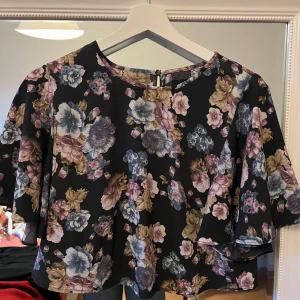 Blommig topp med vida ärmar - Säljer en superfin blommig topp med vida ärmar. Den har en mörk bas med blommor i rosa, blått och beige. Perfekt för vår och höst. Toppen är croppad,Passar både till vardags och fest.