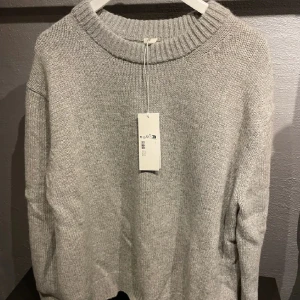 Grå stickad tröja från Arket - Säljer en supermysig grå stickad tröja från Arket i storlek L. Perfekt för kyliga dagar. Tröjan har en klassisk design med ribbad krage och långa ärmar. Pris går att diskutera vid snabb affär!