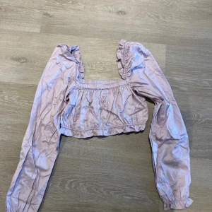 Ljuslila blus med volangdetaljer - Säljer en söt ljuslila blus med volangdetaljer. Den har långa ärmar och en elastisk midja för en bekväm passform. Använd endast 1 gång.