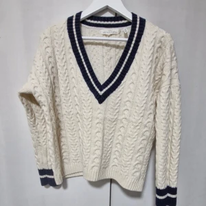 Vit kabelstickad ulltröja från L.O.G.G. - Säljer en superfin vit kabelstickad tröja från L.O.G.G. med mörkblå detaljer. Den har en snygg v-ringning och långa ärmar med ribbade muddar. Perfekt för höst och vinter! Tröjan är i ullblandning vilket gör den både varm och bekväm. Passar perfekt till både jeans och kjol. 🧶✨