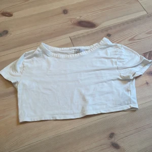 Vit croppad topp från H&M Divided - Säljer en enkel och stilren vit croppad topp från H&M Divided. Perfekt för sommardagar eller som ett basplagg i garderoben. Toppen har korta ärmar och en avslappnad passform. Använd ett fåtal gånger, så den är i bra skick. Passar perfekt till jeans eller kjol!