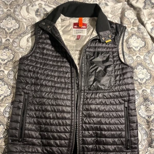 Svart dunväst från Parajumpers - Säljer en svart dunväst från Parajumpers i storlek S. Västen är extra lätt och har en stilren design med dragkedja framtill. Perfekt för höst och vår, och den har praktiska fickor med dragkedjor. Västen är i mycket bra skick och passar både till vardags och lite finare tillfällen.
