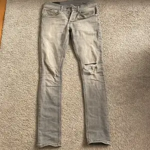 Säljer ett par grå slim jeans ifrån Dondup med modell George i storlek 28. De är i skick 9/10. De har en schysst reva på ena benet. Beninnerlängd 76 cm och midjemått 36 cm. Passar dig som är runt 170-172 cm lång. Hör av dig ifall du har några frågor!