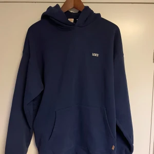 Mörkblå hoodie från Levi's - Säljer en snygg och bekväm mörkblå hoodie från Levi's. Den har en klassisk design med en liten logga på bröstet och en stor ficka framtill. Perfekt för kyliga dagar eller mysiga hemmakvällar. Passar till det mesta i garderoben!