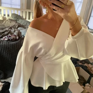 Vit offshoulder blus med knyt - Säljer en superfin vit offshoulder blus med knyt i midjan. Den har långa ärmar och en snygg omlott-design som ger en elegant look. Perfekt för både fest och vardag! 💫