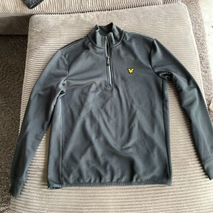 Grå tröja från Lyle & Scott - Säljer en stilren grå tröja från Lyle & Scott i storlek S. Tröjan har en halv dragkedja och det klassiska gula logotypmärket på bröstet. Hör av dig vid fler frågor!