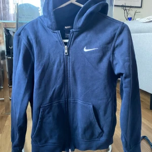 Mörkblå hoodie från Nike - Säljer en snygg mörkblå hoodie från Nike i storlek 158(?) passar 12-15 år. Den har en dragkedja framtill och en Nike-logga på bröstet