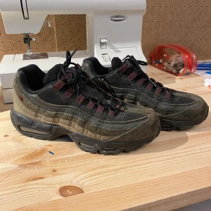 Nike Air Max 95 i grönt och svart - Säljer ett par Nike Air Max 95 i grönt och svart. Skorna har en cool design med snörning och en robust sula. Perfekta för både vardag och träning. De är i bra skick med lite slitage på sulan, men fortfarande superbekväma och snygga!