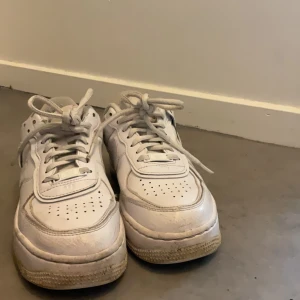 Vita Nike Air Force sneakers - Säljer ett par vita Nike Air Force sneakers i acceptabelt skick. De har en klassisk design med snörning och en robust sula. Perfekta för vardagsbruk och ger en stilren look. Lite smuts på sulan men annars i fint skick.