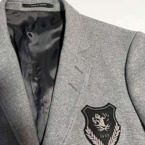 Grå Blazer från Tiger of Sweden - Snygg grå kavaj från Tiger of Sweden i mycket bra skick. Den har ett stilrent emblem på bröstet och är fodrad med ett prickigt mönster. Perfekt för både formella och semi-formella tillfällen. Kavajen har två knappar framtill och en klassisk passform.