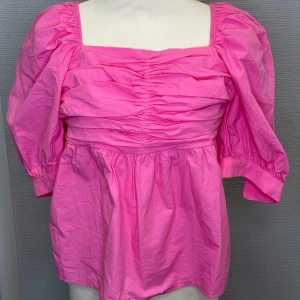 Rosa blus med puffärmar - Säljer en superfin rosa blus med puffiga trekvartsärmar och rynkade detaljer framtill. Perfekt för både vardag och fest! Den har en fyrkantig halsringning och är gjord i ett lätt och bekvämt material. Passar perfekt till jeans eller kjol för en söt look.
