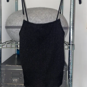 Svart glittrig ribbad topp - Snygg svart ribbad topp med smala axelband från Zara. Perfekt för en utekväll eller fest. Den har en tight passform som framhäver figuren. 