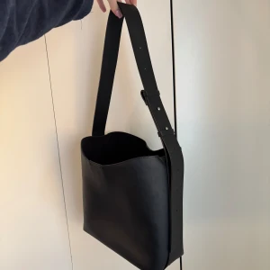 Svart axelväska  - Stilren svart axelväska i skinnimitationfrån Lindex (köpt på zalando för 500 kr). Perfekt för vardagsbruk med justerbar axelrem. Den är väldigt rymlig, använd men i mycket bra skick.  Mått: 31x31x13