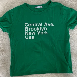 Grön t-shirt från Zara - Säljer en grön OANVÄND t-shirt från Zara med tryck 'Central Ave. Brooklyn New York Usa' i vitt. T-shirten är i bomull och har korta ärmar. Står storlek M på tröjan men passar även folk som bär S! 