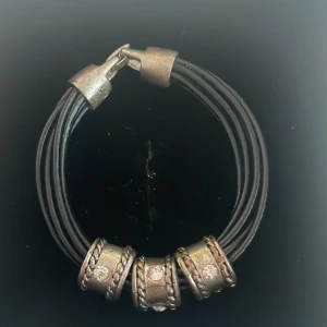 Svart armband med silverdetaljer - Snyggt svart armband med flera remmar och coola silverdetaljer. Armbandet har tre silverringar med glittriga stenar som ger en extra touch. Perfekt för att piffa upp vilken outfit som helst! Lås i silverfärg för säker passform.