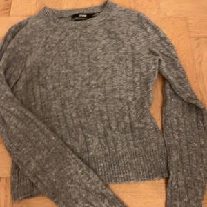 Grå stickad tröja från bikbok - Säljer en stilren grå stickad tröja från BikBok Tröjan har en ribbad struktur och långa ärmar, perfekt för kyligare dagar. Passar bra till både jeans och kjol. 