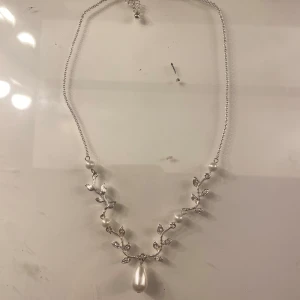 Elegant halsband med pärlor och lövdetaljer - Ett vackert halsband i silverfärg med delikata lövdetaljer och en stor pärla som hänge. Perfekt för att ge en elegant touch till din outfit.