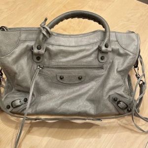 Grå axelväska med dragkedja handväska - Snygg grå axelväska i skinn med praktisk dragkedja framtill. Väskan har dubbla handtag och en justerbar axelrem för bekväm användning. Perfekt för att bära med sig det nödvändigaste med stil.