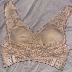 Beige spets-bh - Säljer en elegant beige bh med spetsdetaljer. Den har justerbara hakar i ryggen och är tillverkad i 93% nylon och 7% elastan för en bekväm passform. 