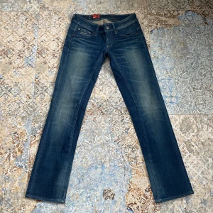 Blå jeans från G-Star - Snygga blå jeans från G-Star med en klassisk femficksdesign och knappgylf. De har en lätt tvättad look och raka ben. Midjemått:ca 36 cm rakt över. Innerbenslängden: 77cm