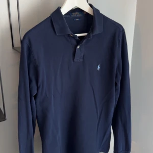 Mörkblå pikétröja från Ralph Lauren - Säljer en klassisk mörkblå lång pikétröja från  Ralph Lauren, mycket bra skick! Storlek M.               