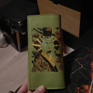 Grön plånbok med konstmotiv - Unik grön plånbok med ett konstnärligt motiv på framsidan. Plånboken har en dragkedja på baksidan och flera fack inuti för kort och kontanter. Perfekt för dig som vill ha något annorlunda och stilfullt.