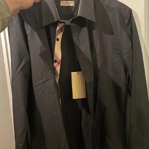 Svart skjorta från Burberry - Snygg svart skjorta från Burberry med klassiskt rutigt mönster på insidan av kragen. Skjortan är i storleken L men passar M. Har ni några funderingar så är det bara att fråga ☺️