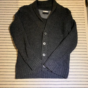 Mörkgrå stickad kofta med knappar - Säljer en stilren mörkgrå stickad kofta med knappar framtill. Koftan har en klassisk design med ribbade detaljer och långa ärmar. Perfekt för kyliga dagar. Kan skicka bild med plagget på. (Pris kan diskuteras)
